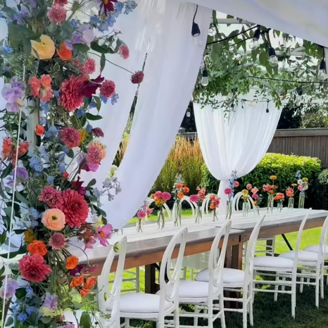 This image shows a beautiful table setting inside a tent with exquisite vibrant floral decor.
